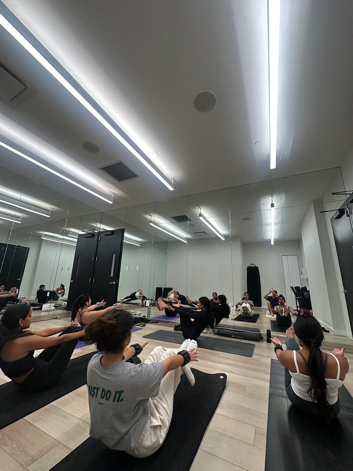 Students holding boat pose in a bright mirrored studio