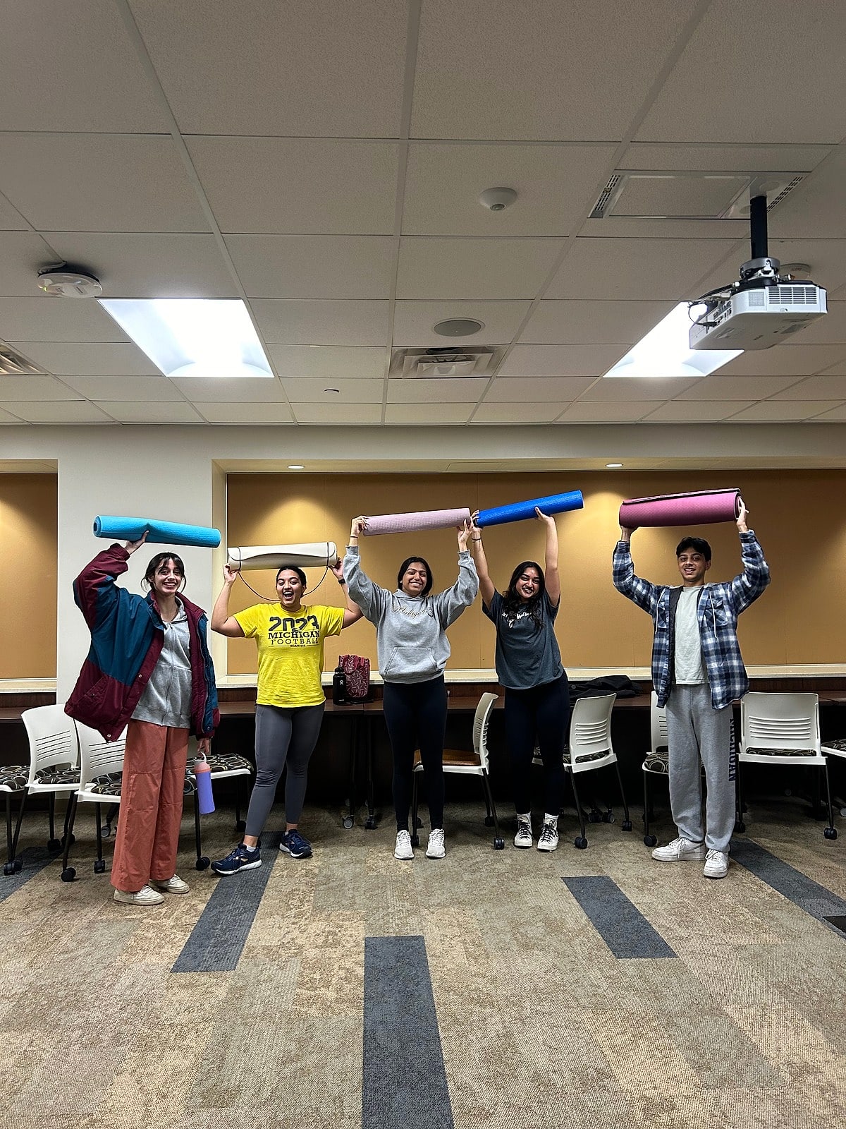 Students holding their rolled yoga mats over their heads after class
