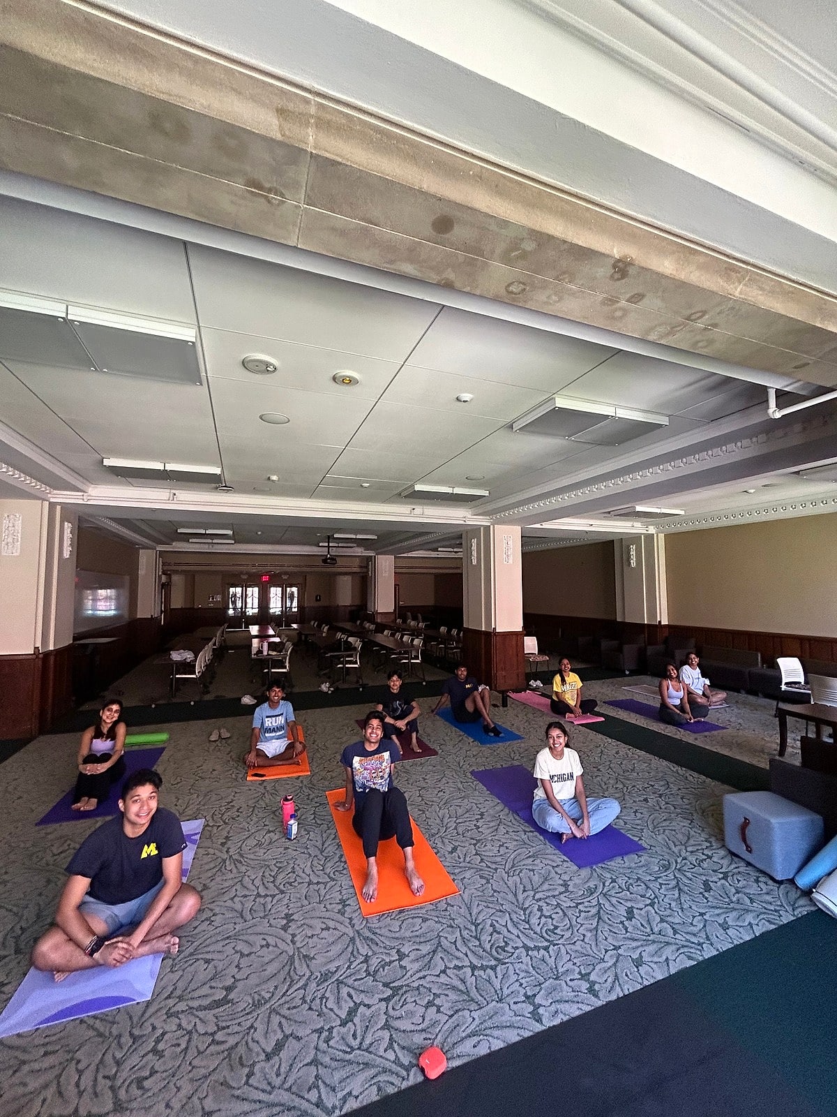 Students on colorful mats in a large hall with tall windows
