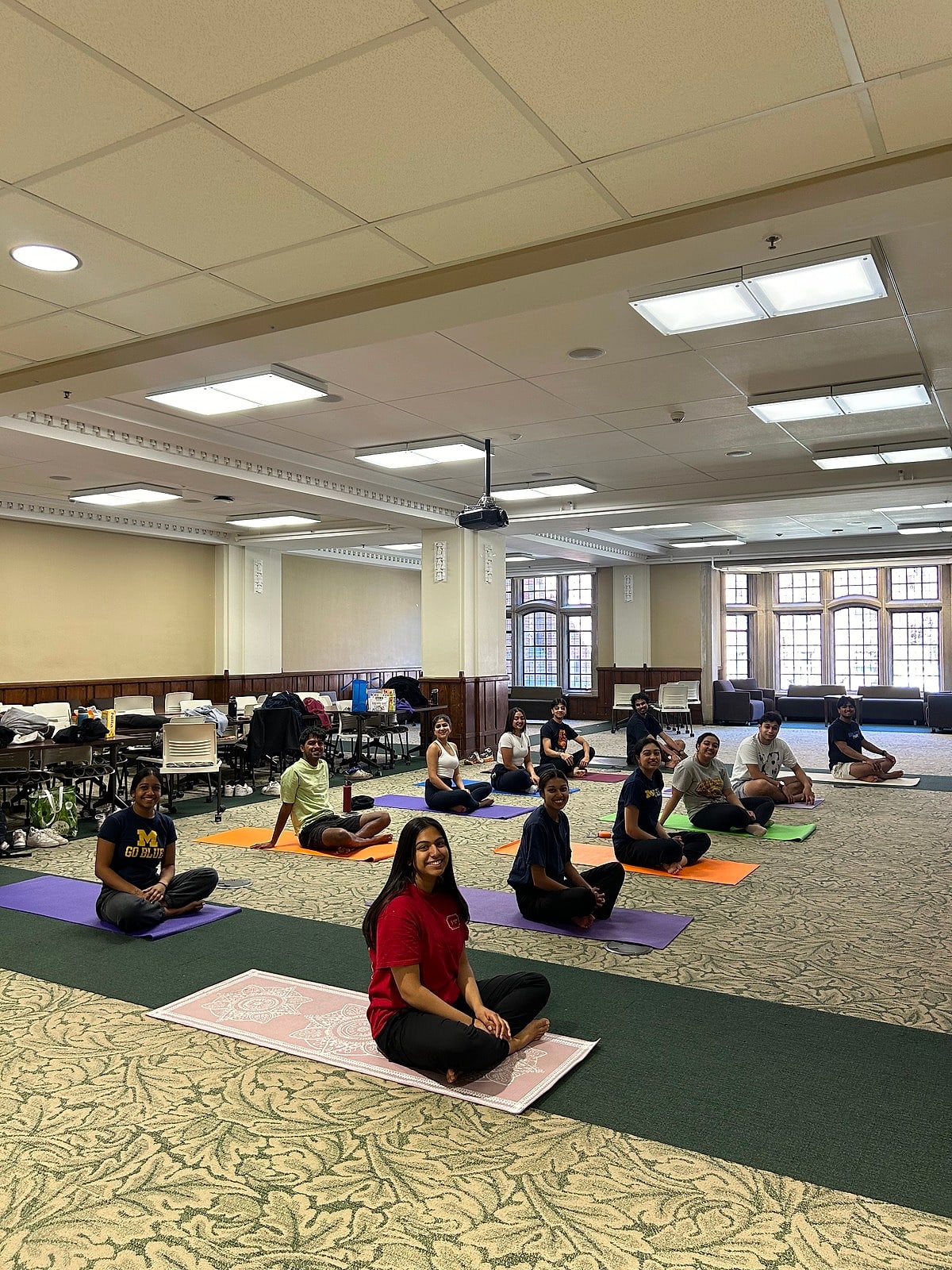 A class seated on mats spread across a sunny hall