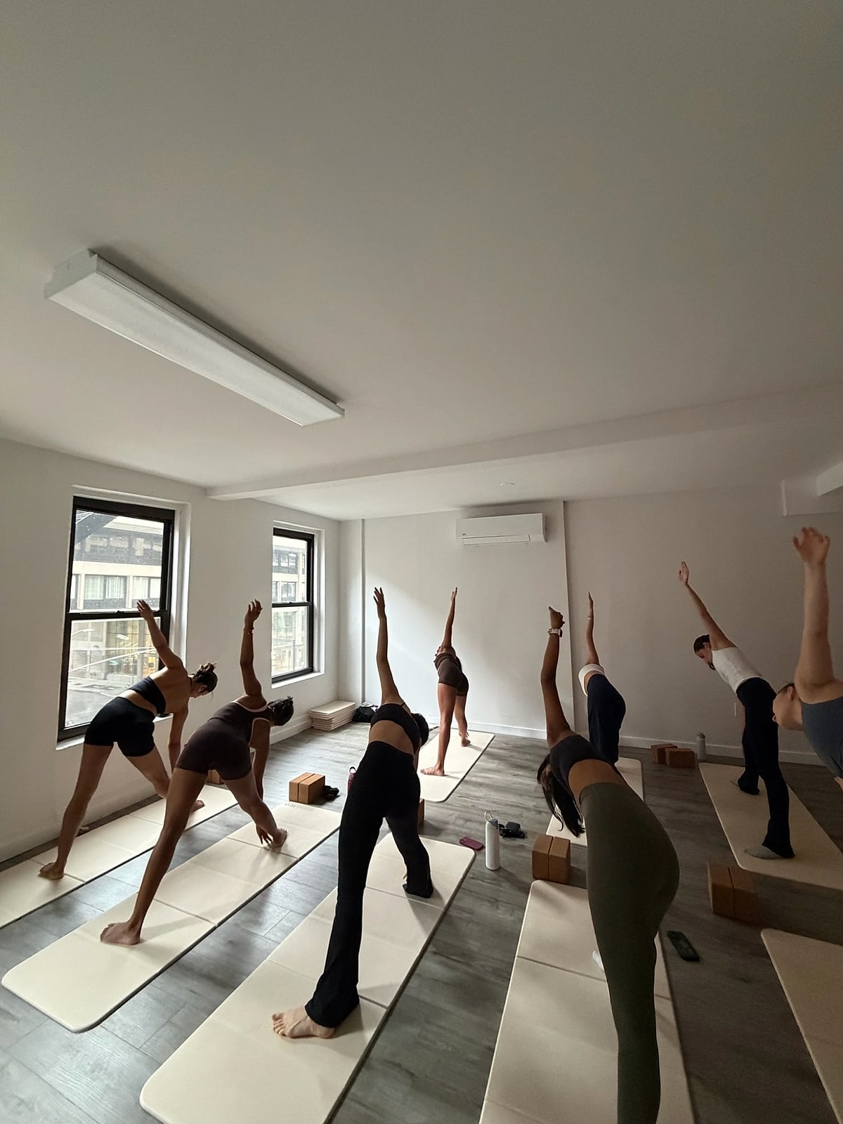 A full class in triangle pose on cream mats in a bright studio with tall windows