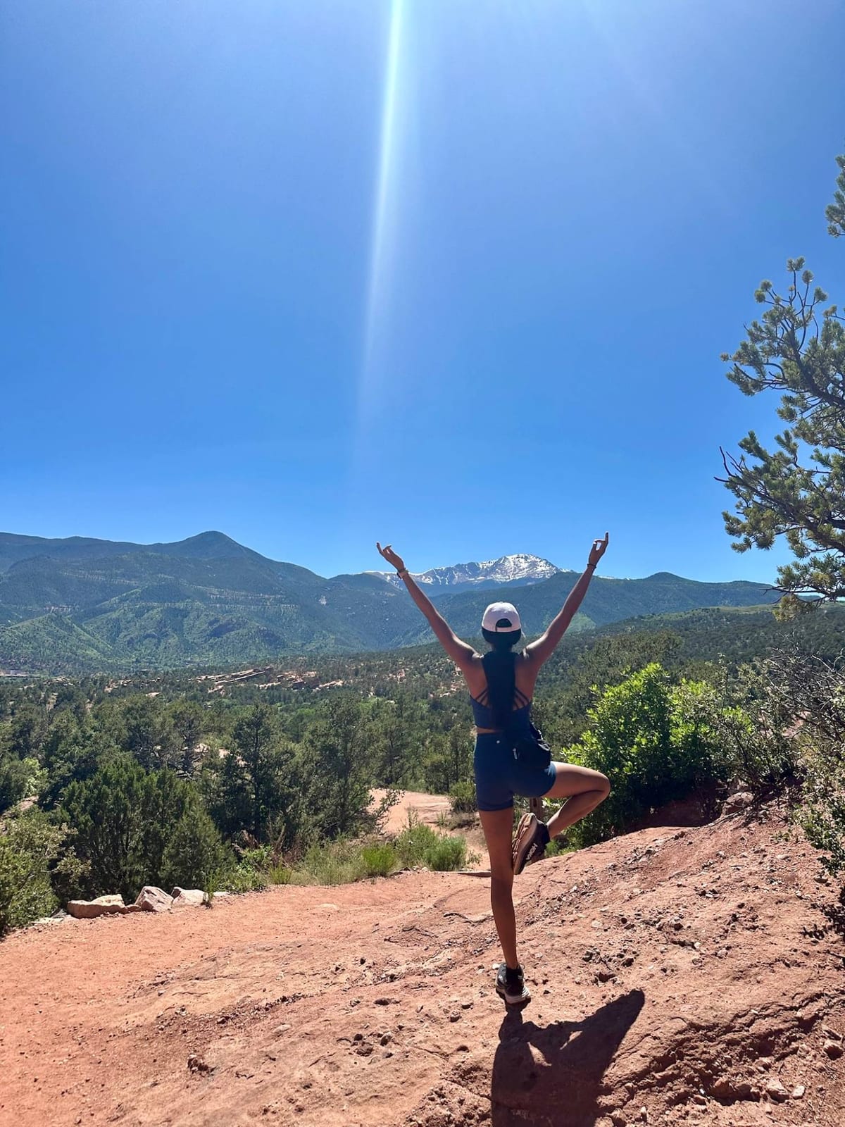 Saniya in tree pose with arms raised on a red-rock trail, mountains behind