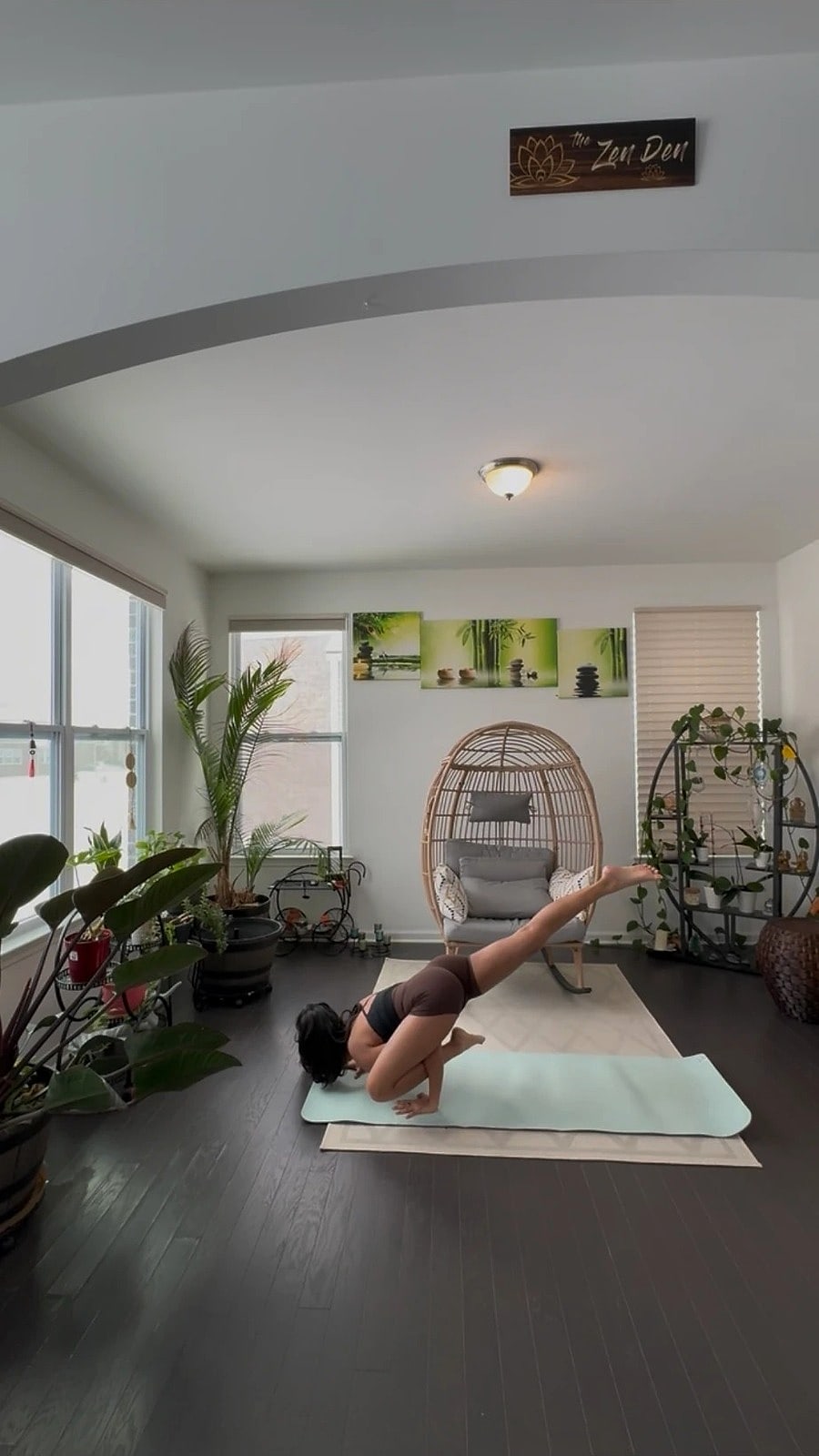 Saniya in a crow pose variation on a mint mat in a sunny room full of plants