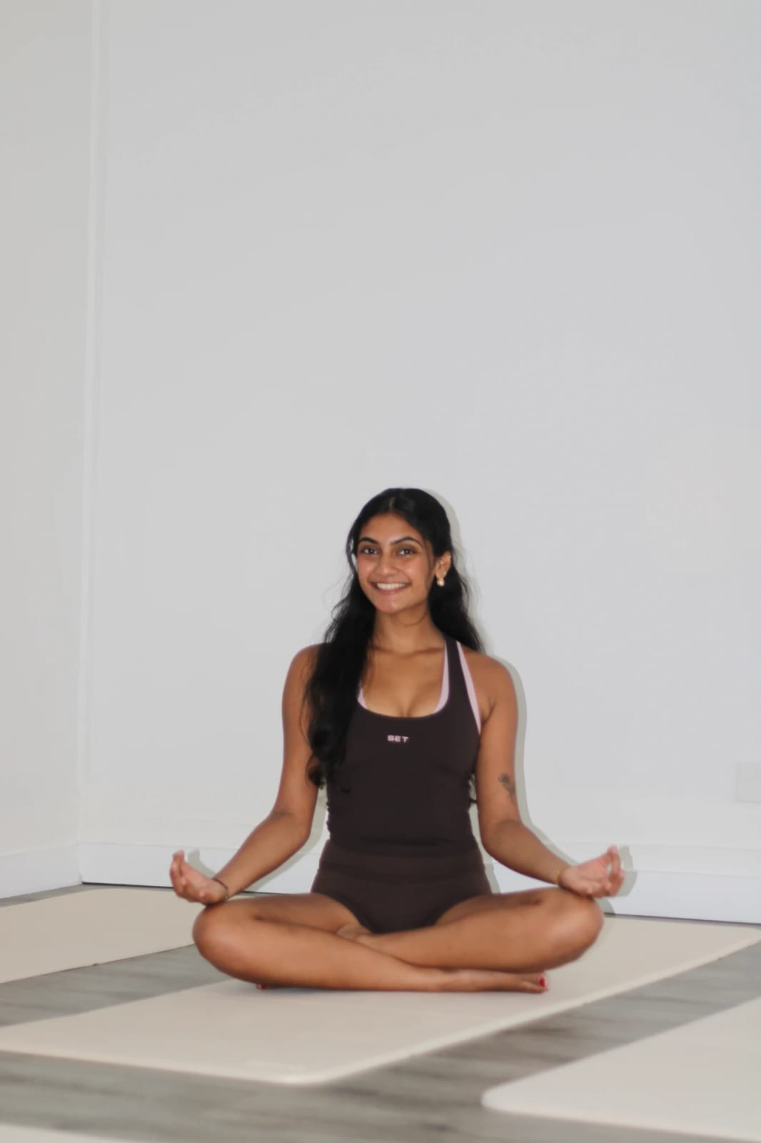 Saniya sitting cross-legged in easy pose on a yoga mat, smiling