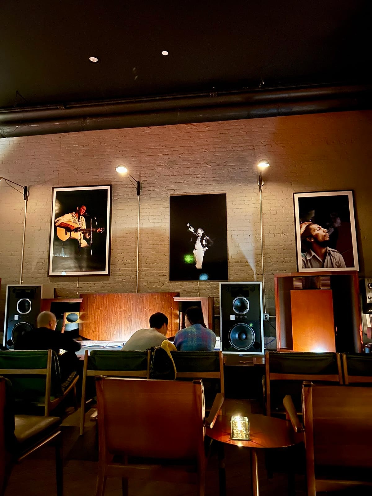 A dim listening bar with big speakers, framed jazz photos and armchairs