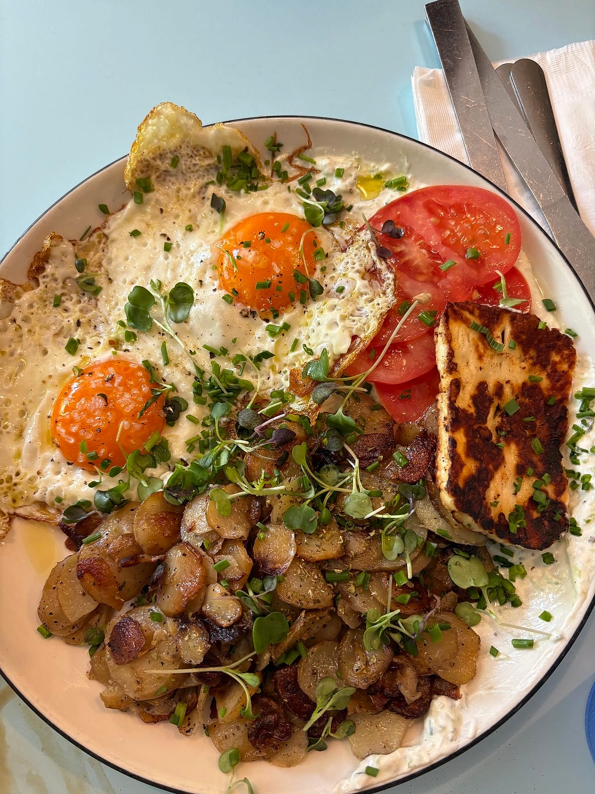 A Greek breakfast plate of fried eggs, grilled halloumi, potatoes and tomatoes