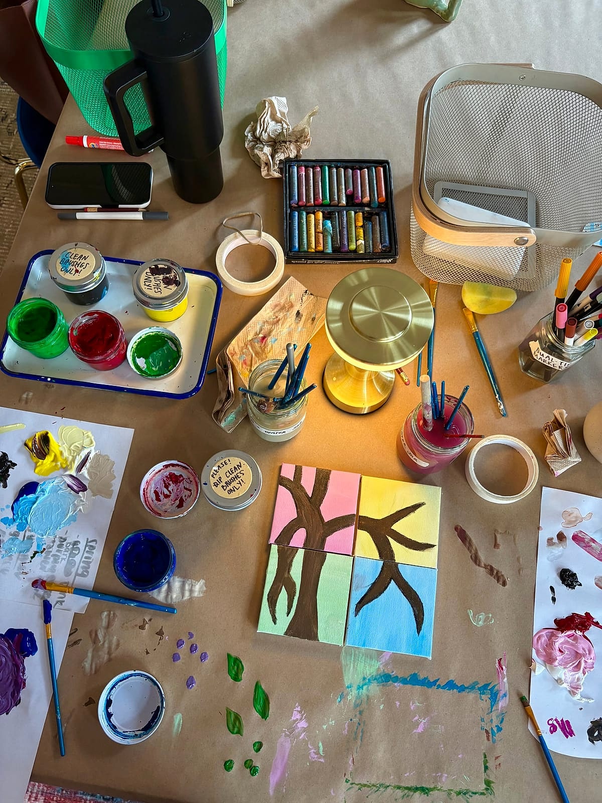 A table covered in paints, brushes and a half-finished painting