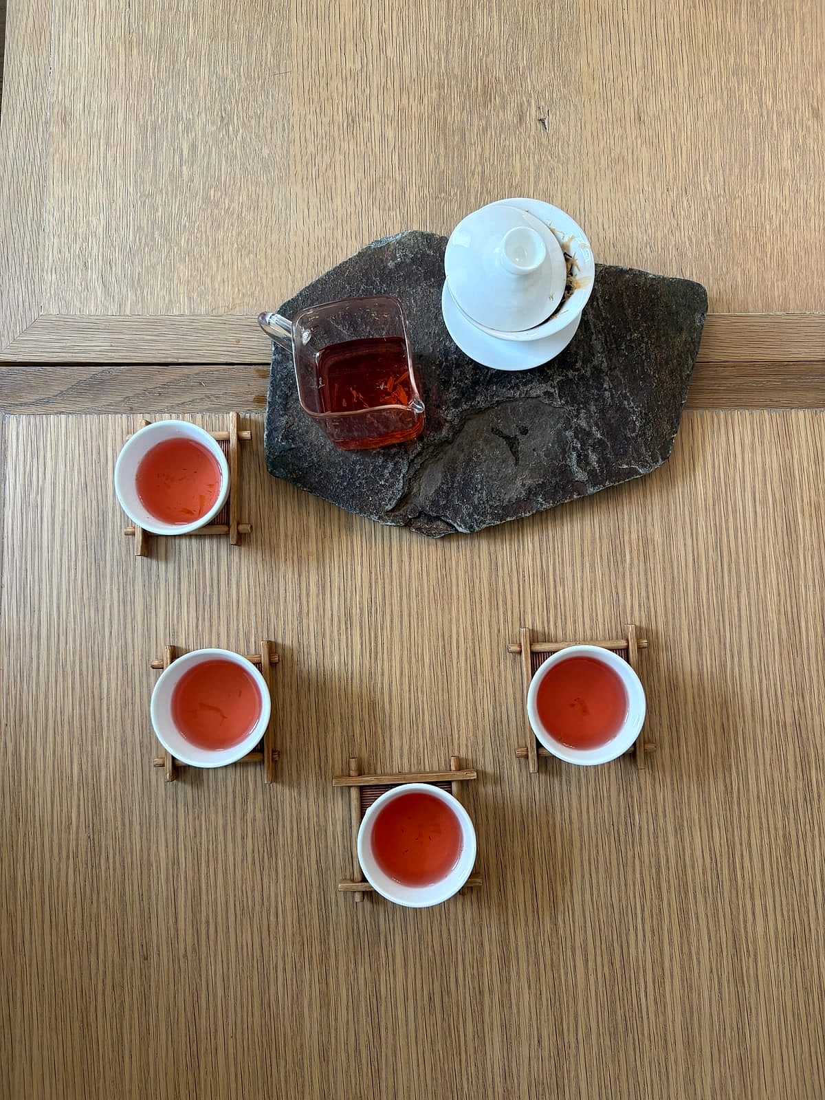 Cups of tea poured for four around a teapot on a stone tray