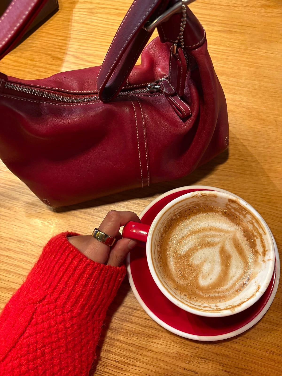 A latte in a red cup, held next to a red leather bag