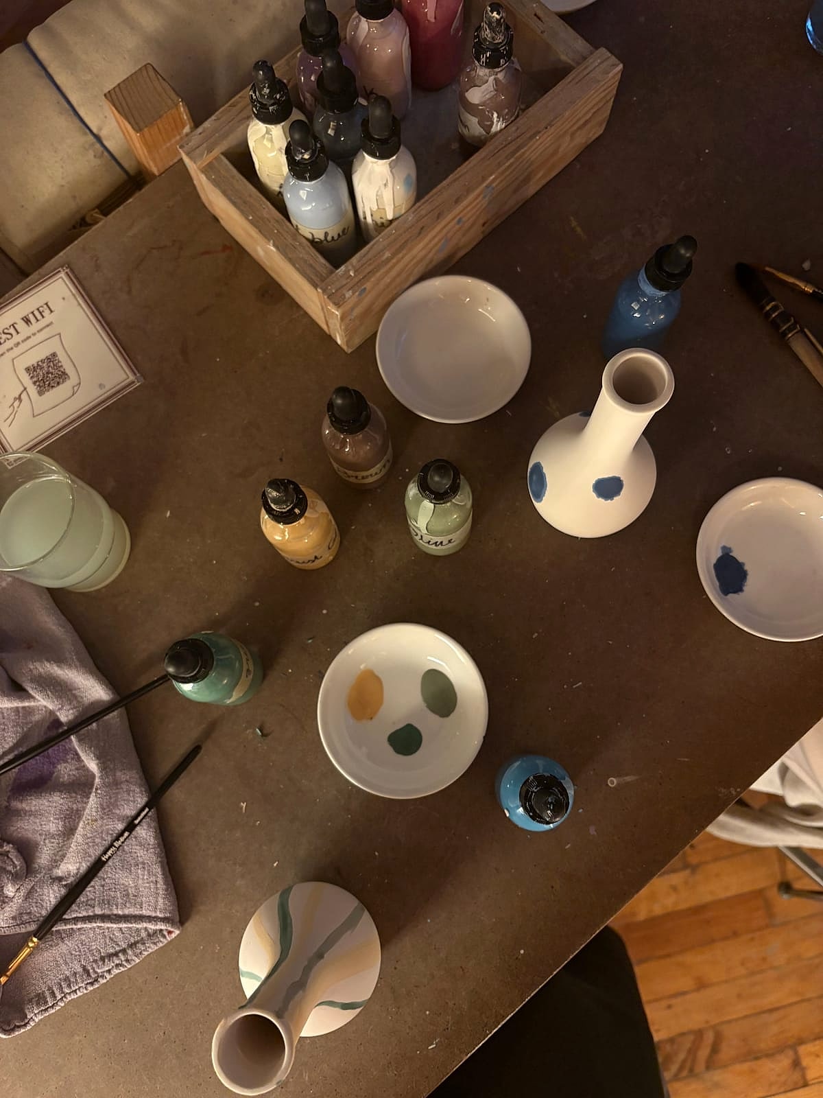 A table set with paints, brushes and ceramic pieces ready to paint