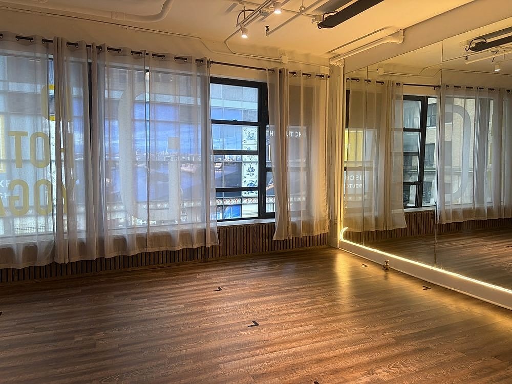 An empty studio with sheer curtains over tall windows and a warm wood floor