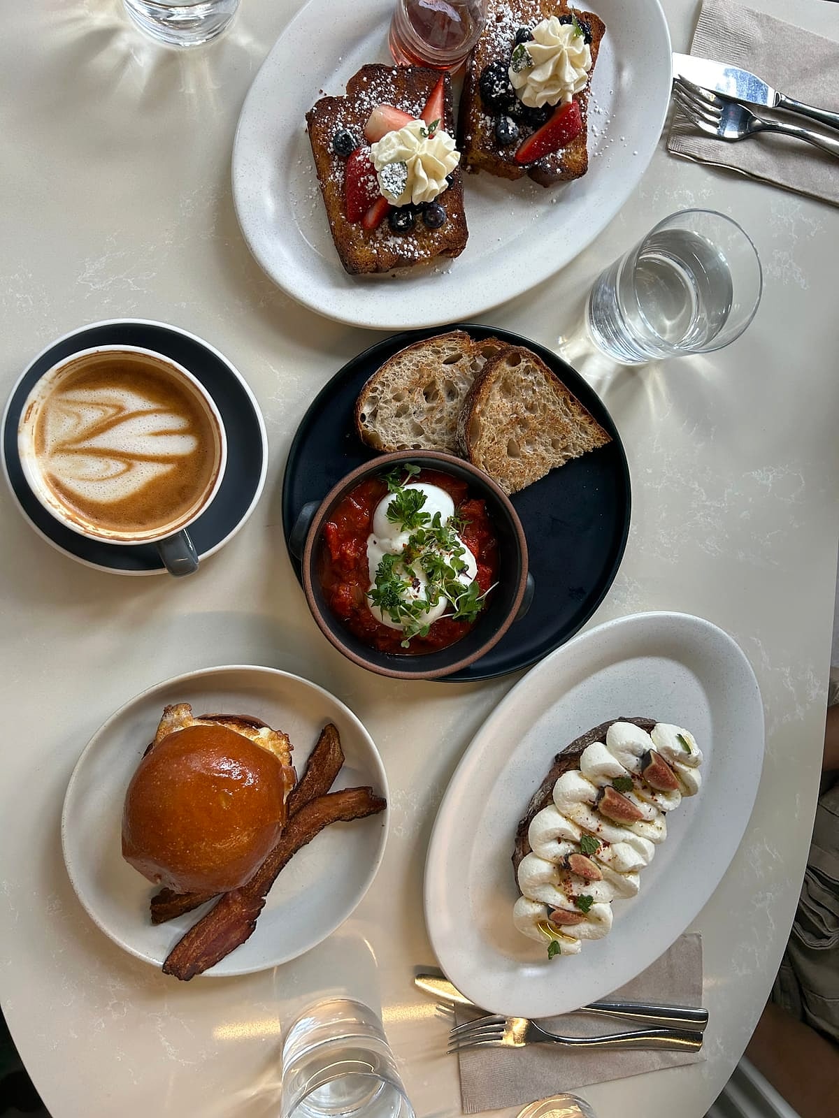 A brunch spread of French toast, a breakfast sandwich, shakshuka and lattes