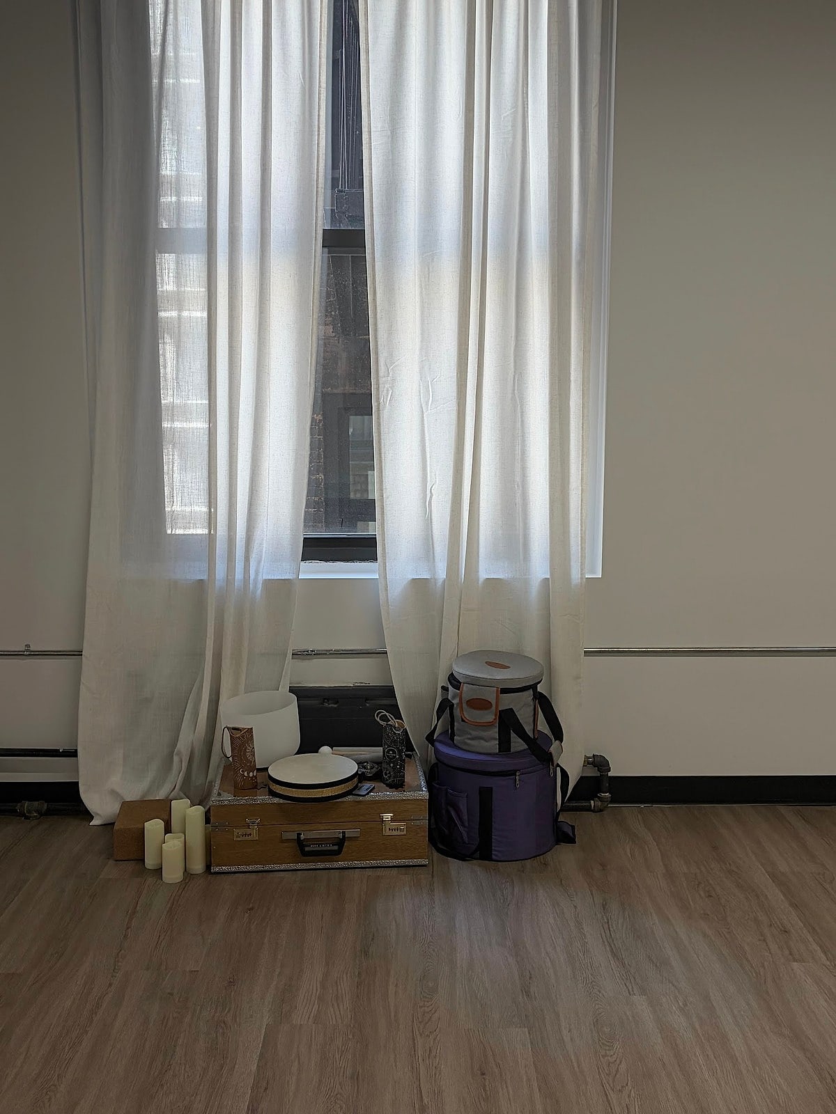 A sunlit corner with sheer curtains, a sound-bath bowl and candles