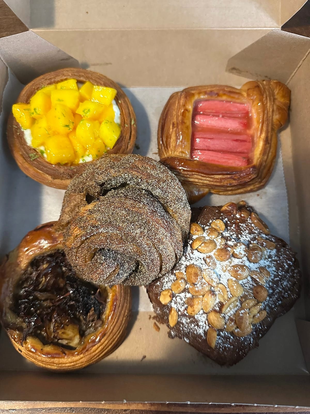 A box of laminated pastries, from fruit danishes to a sesame bun