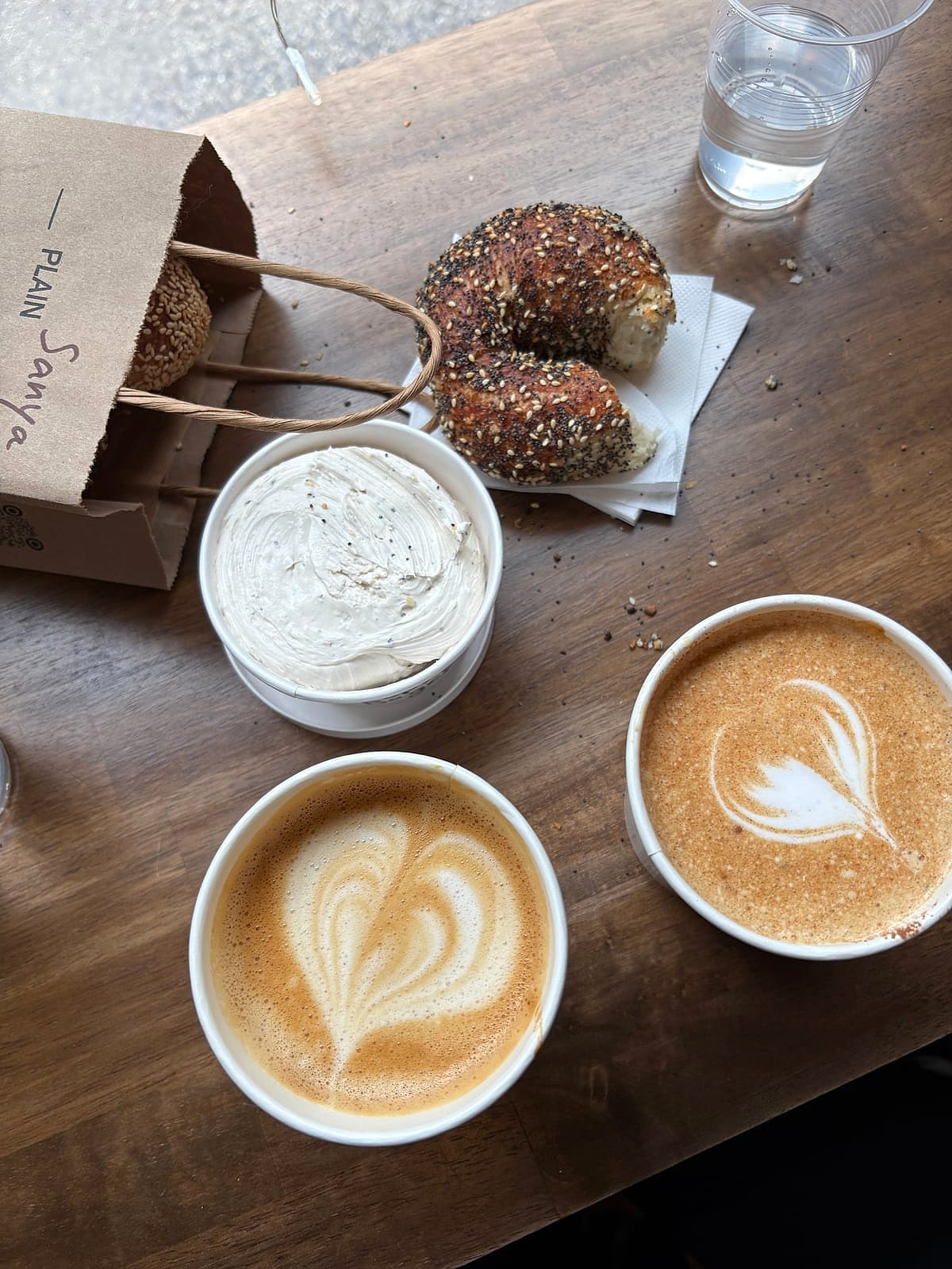 Two lattes beside sesame bagels and a tub of cream cheese