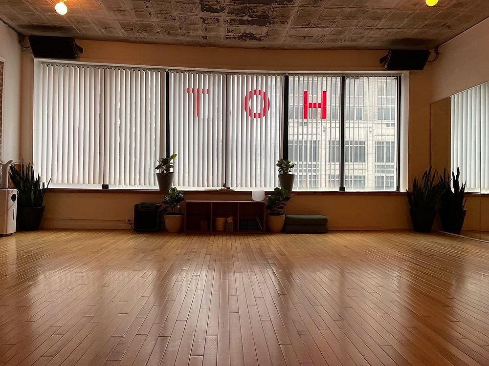 Sunlight through tall window blinds onto a warm wooden studio floor