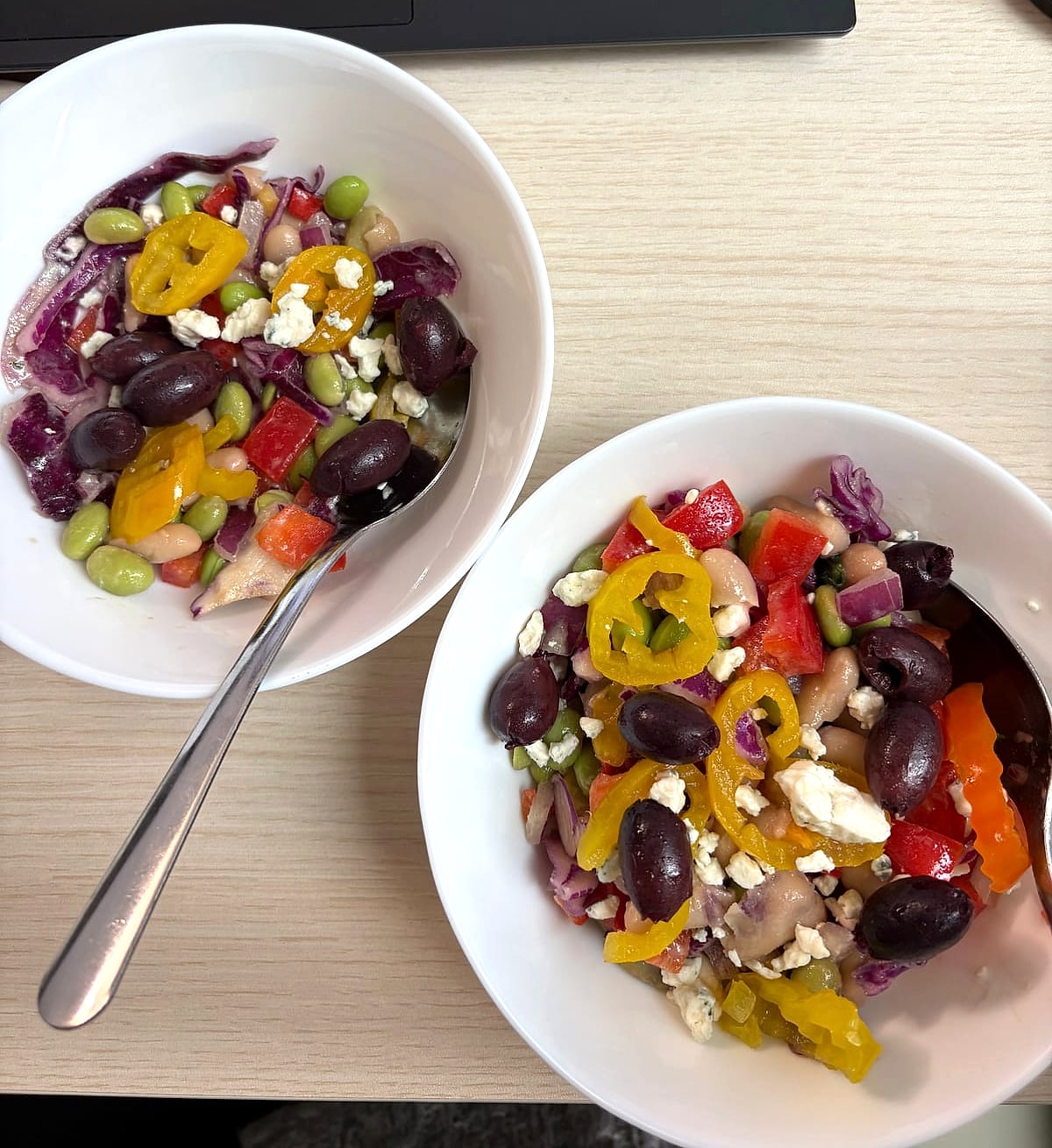Two bowls of bean salad with edamame, olives, peppers and red cabbage