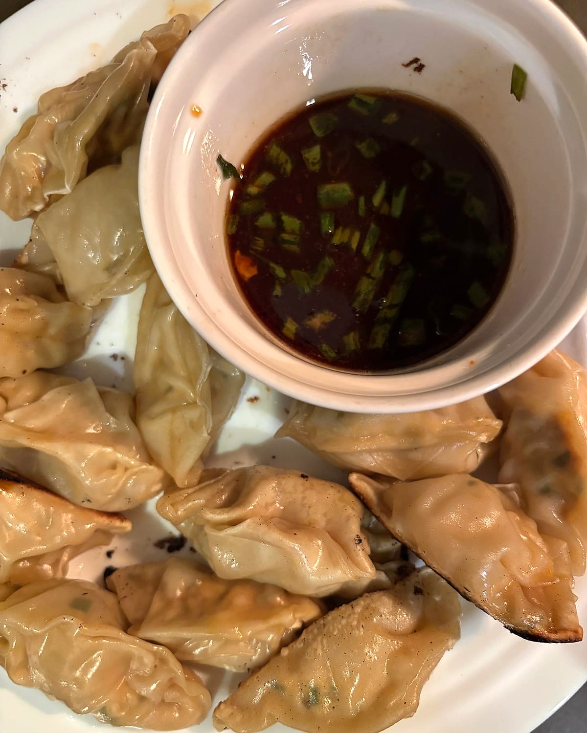 Pan-fried dumplings on a plate with a bowl of soy dipping sauce and scallions