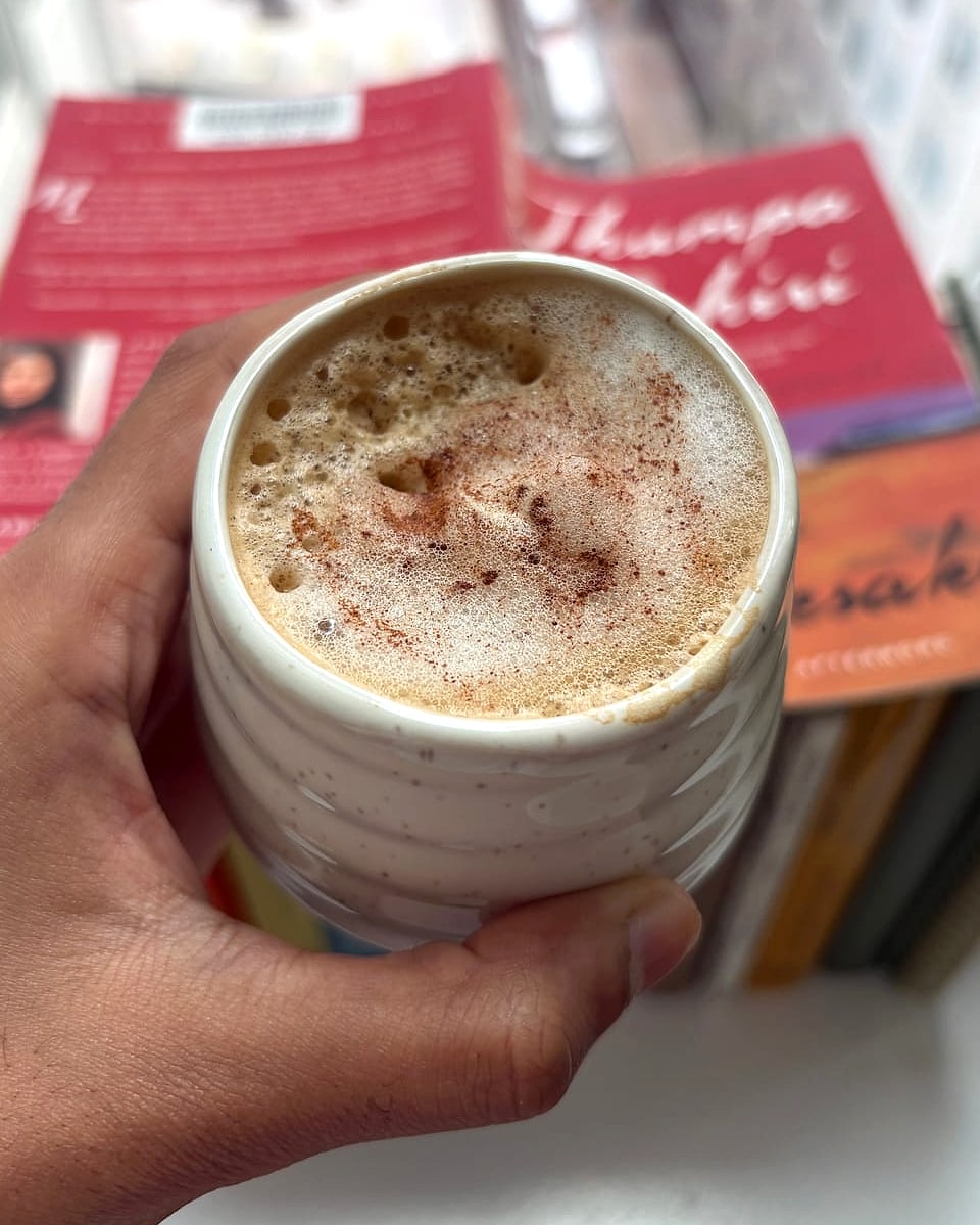 A cortado dusted with cinnamon, held up in front of a stack of books