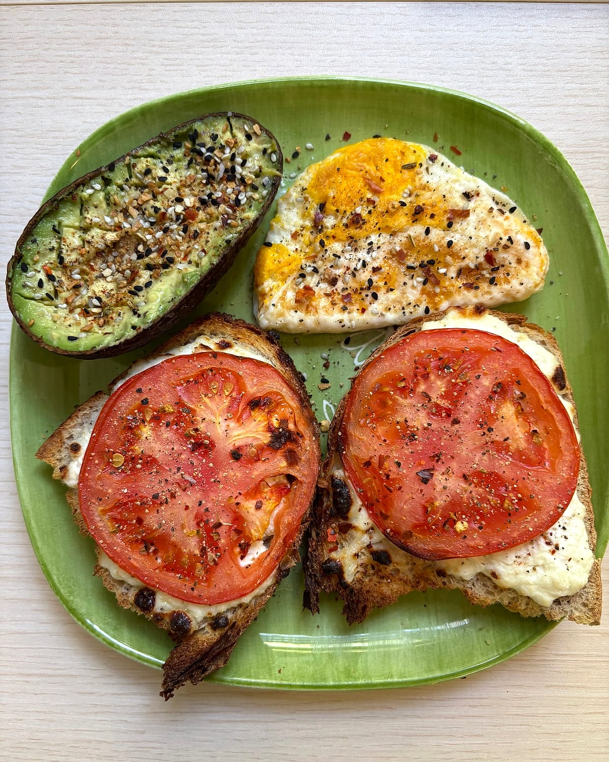 Two slices of cottage cheese and tomato toast with half an avocado and a fried egg on a green plate