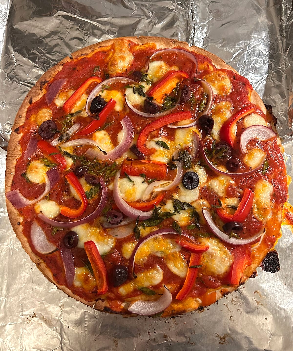 A gluten-free pizza topped with red onion, peppers, olives and melted mozzarella