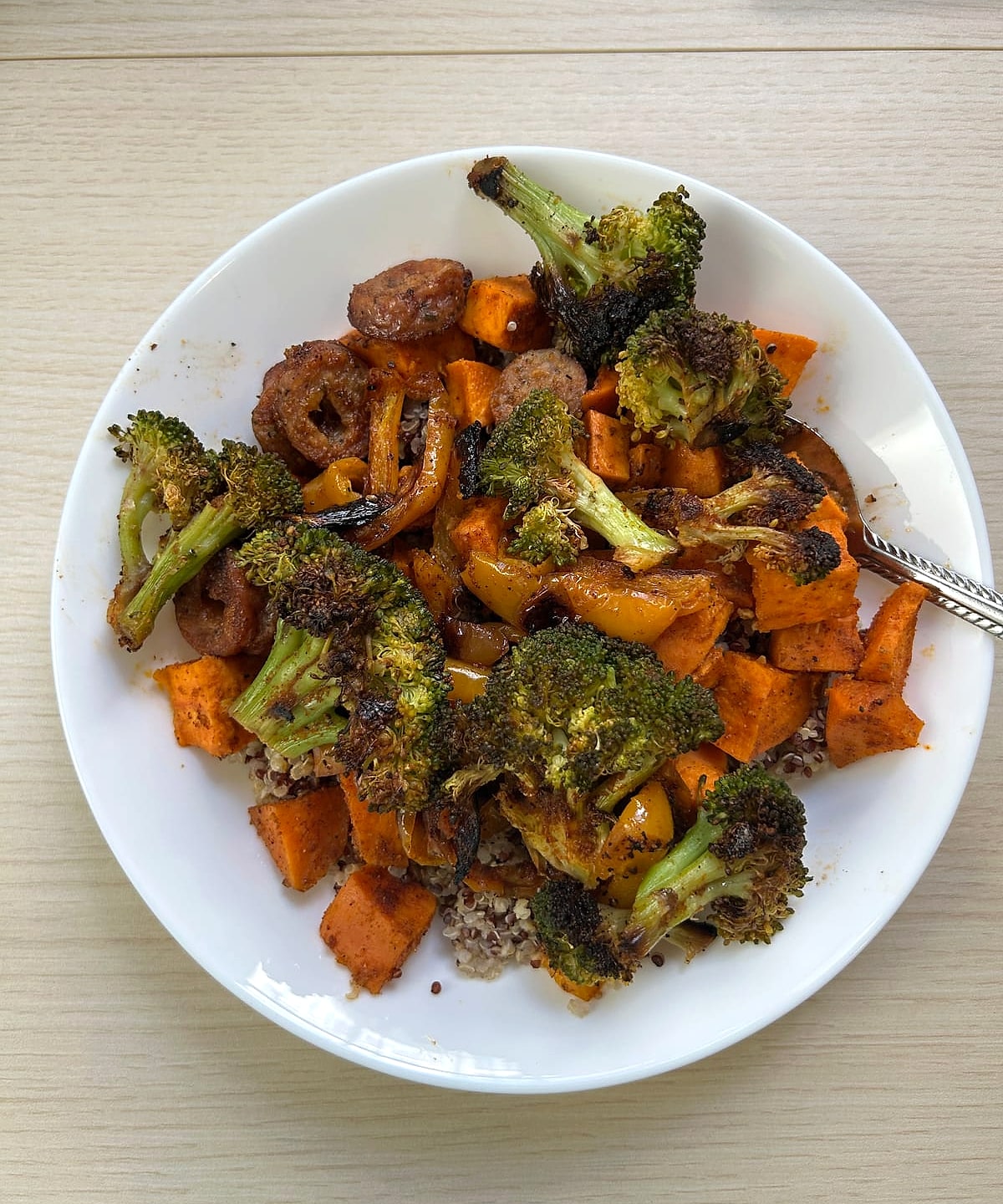 A bowl of roasted broccoli, peppers and sliced sausage over quinoa
