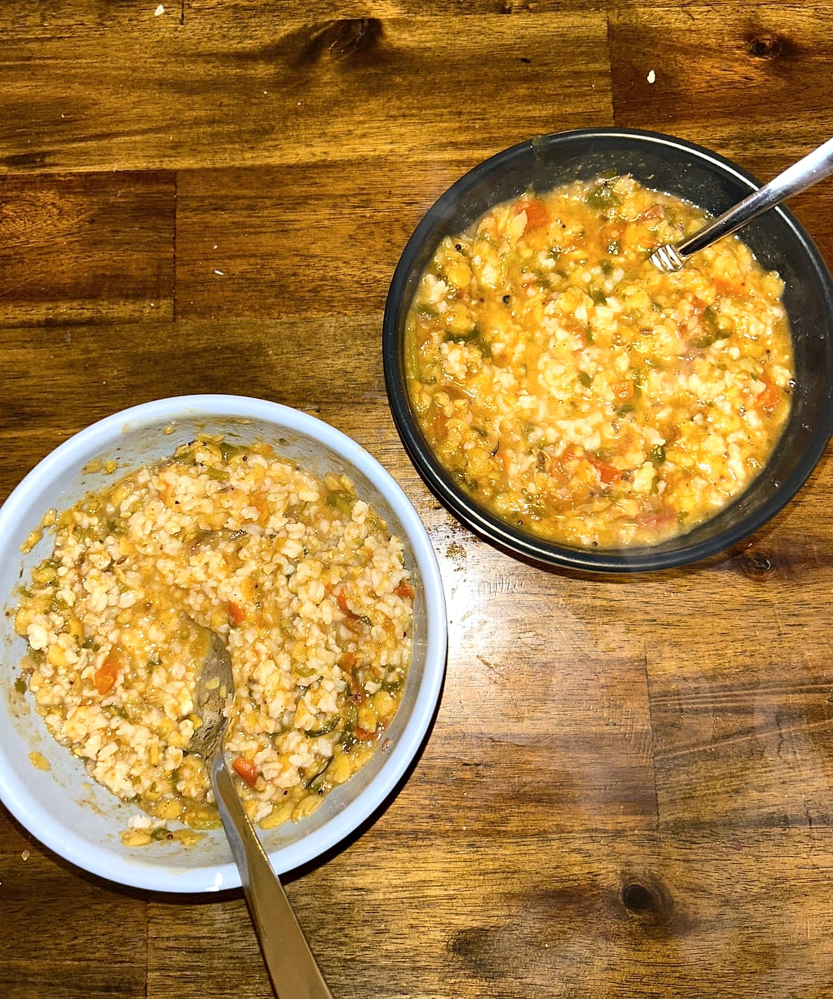 Two bowls of rasam with rice on a wooden table