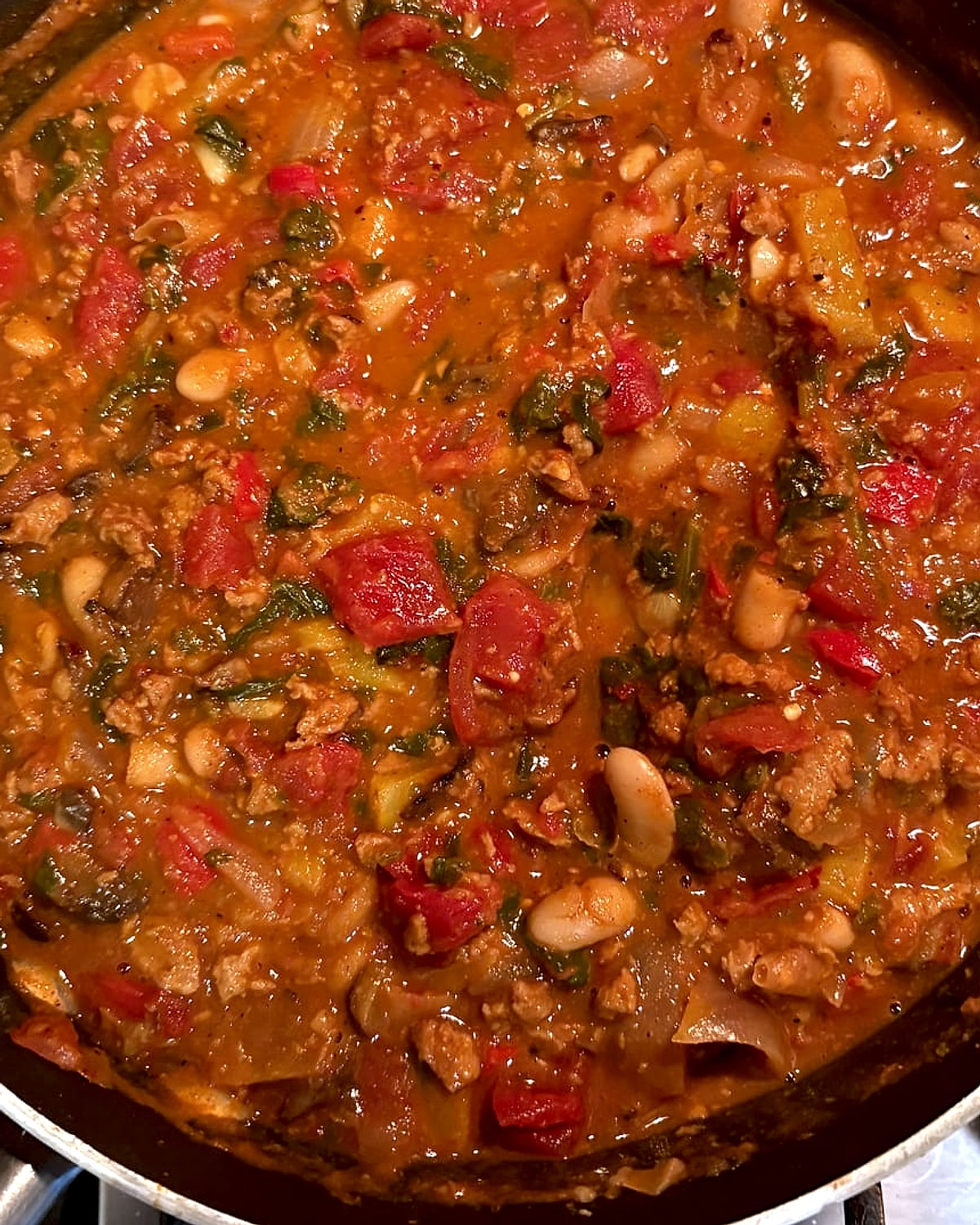 A pan of vegan chili with beans, tomatoes, peppers and greens